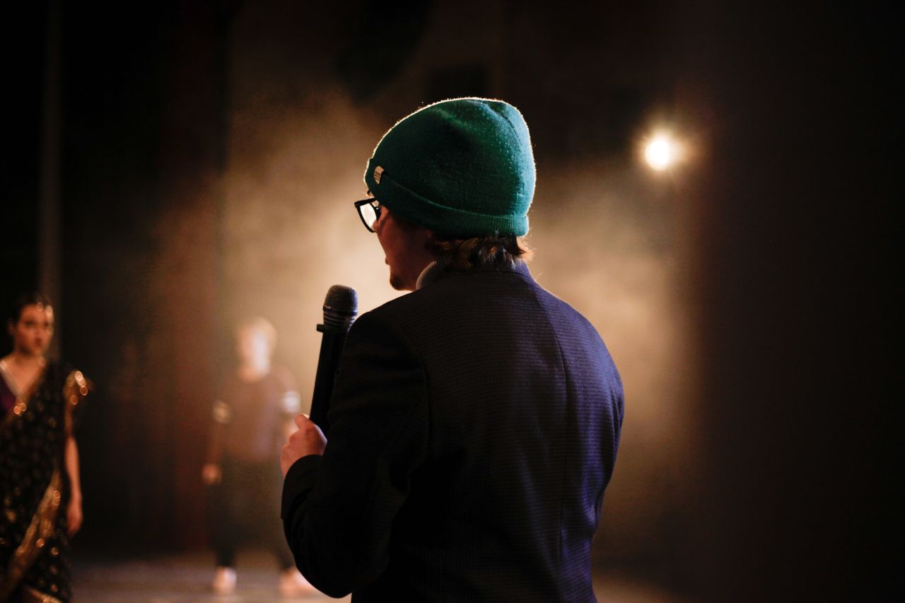 Jak zacząć stand-up? Twój pierwszy występ na Open Mic Moody scene of a performer holding a microphone under a spotlight on stage.